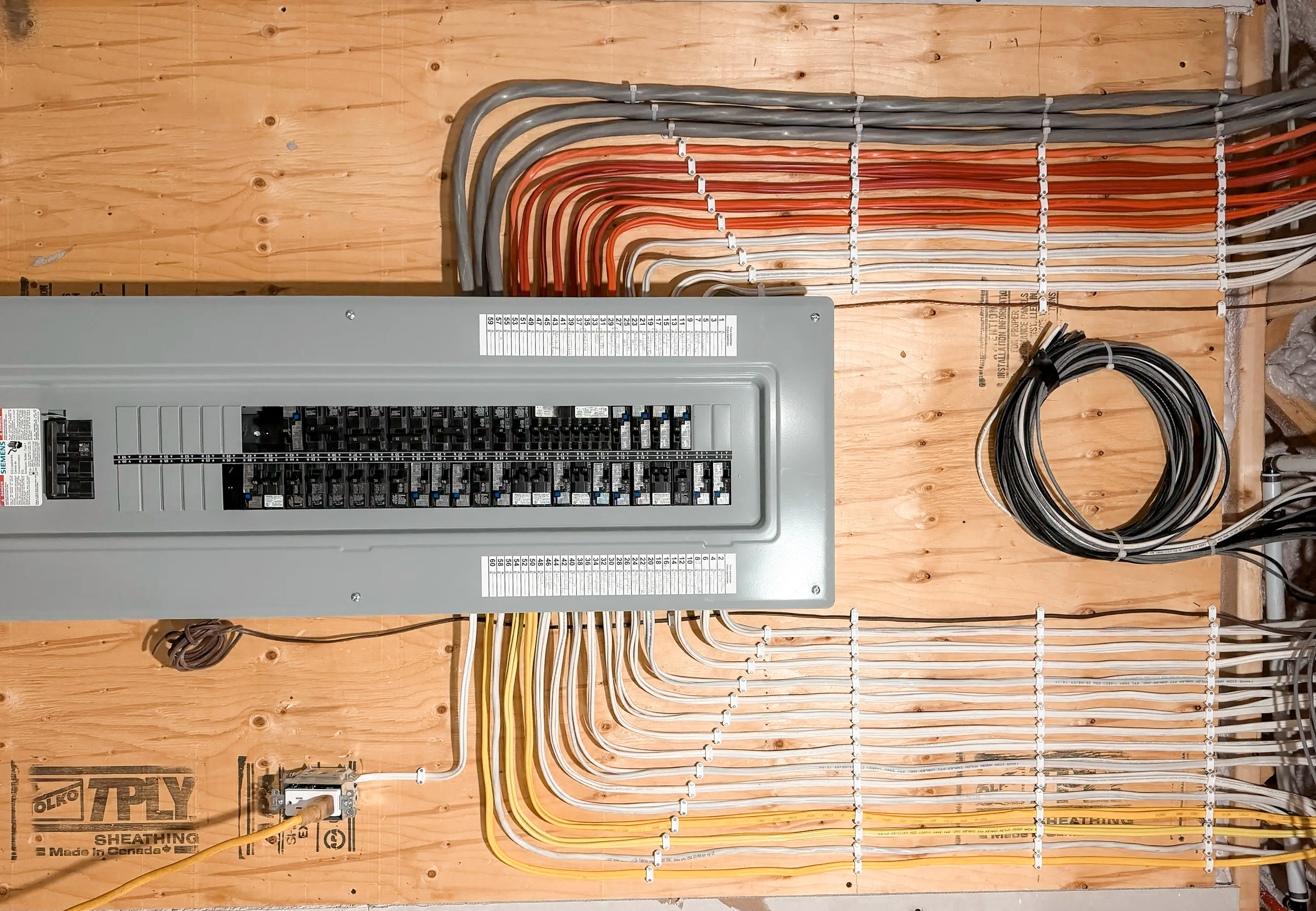 Residential electrical panel with multi-coloured wiring organized on a plywood wall