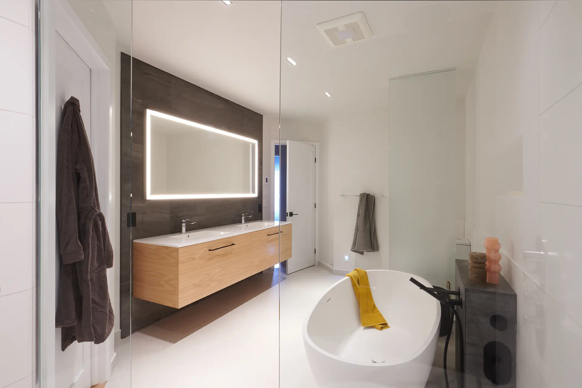 Modern bathroom with white freestanding bathtub, floating light wood vanity, backlit mirror, and contrasting accent walls.