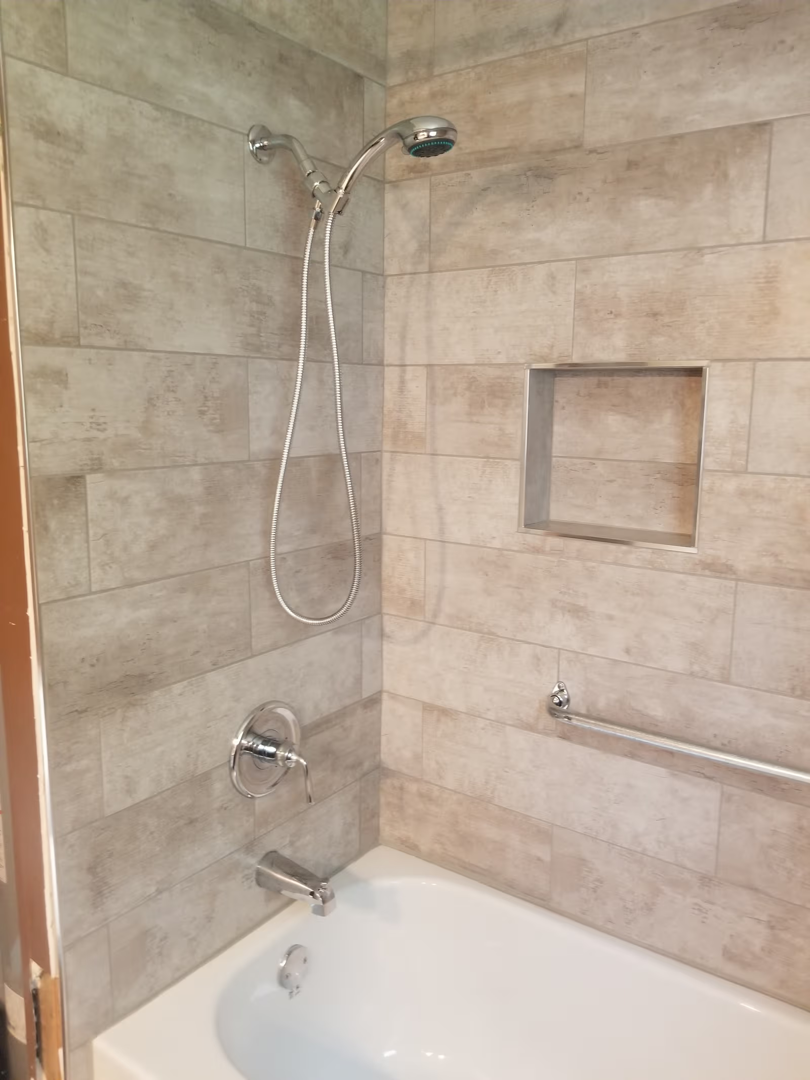 Tub-shower with beige tile, chrome showerhead, wall niche and grab bar