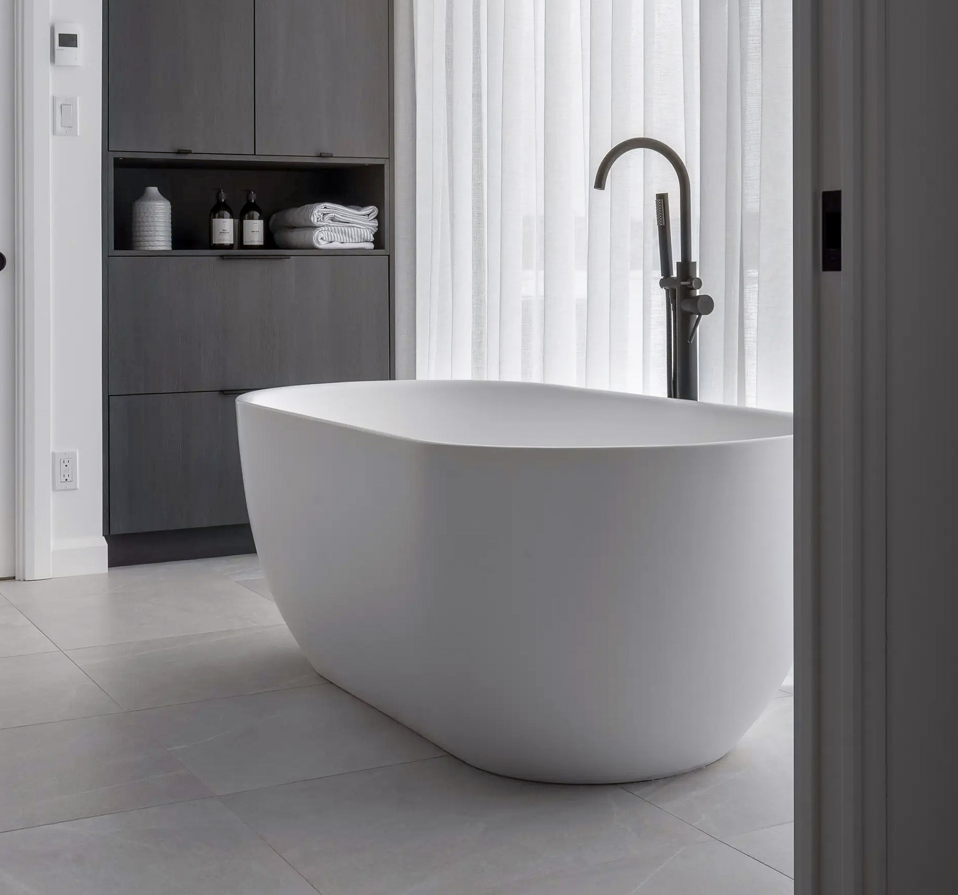 Salle de bain moderne avec baignoire autoportante blanche et robinetterie noire mate.