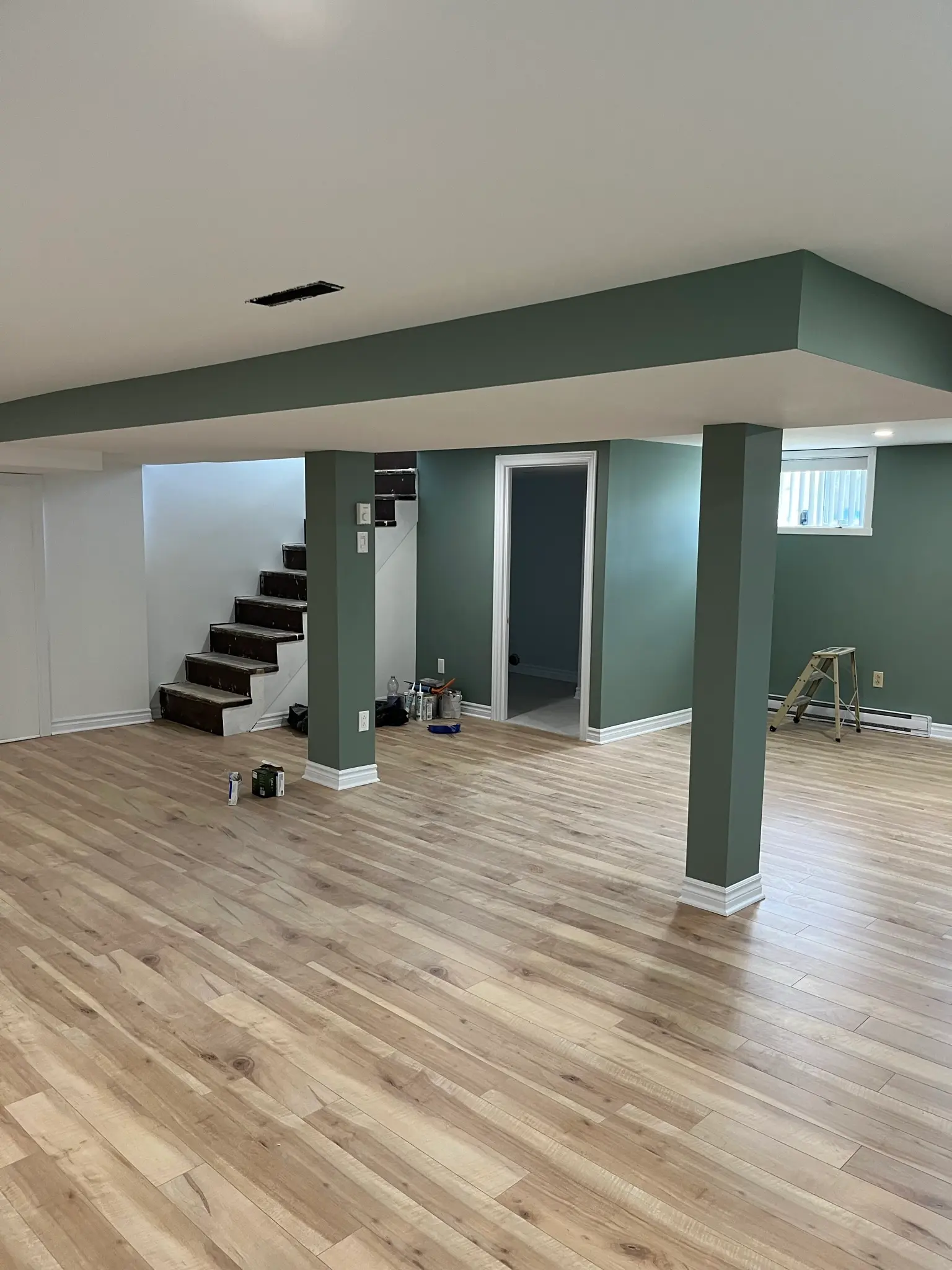 Renovated basement with sage green walls, wood-look flooring, painted columns, staircase and recessed ceiling lighting