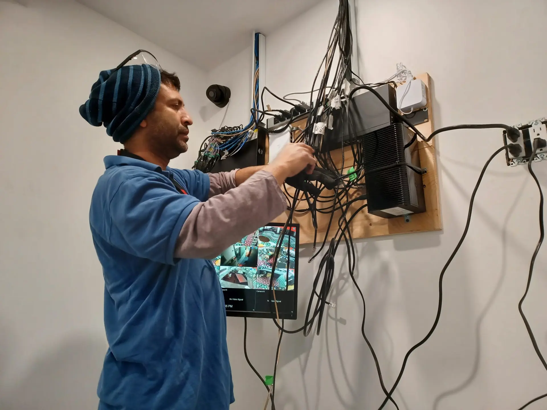 Technician installing a security camera system with network wiring, electronic equipment, and a video monitoring screen.