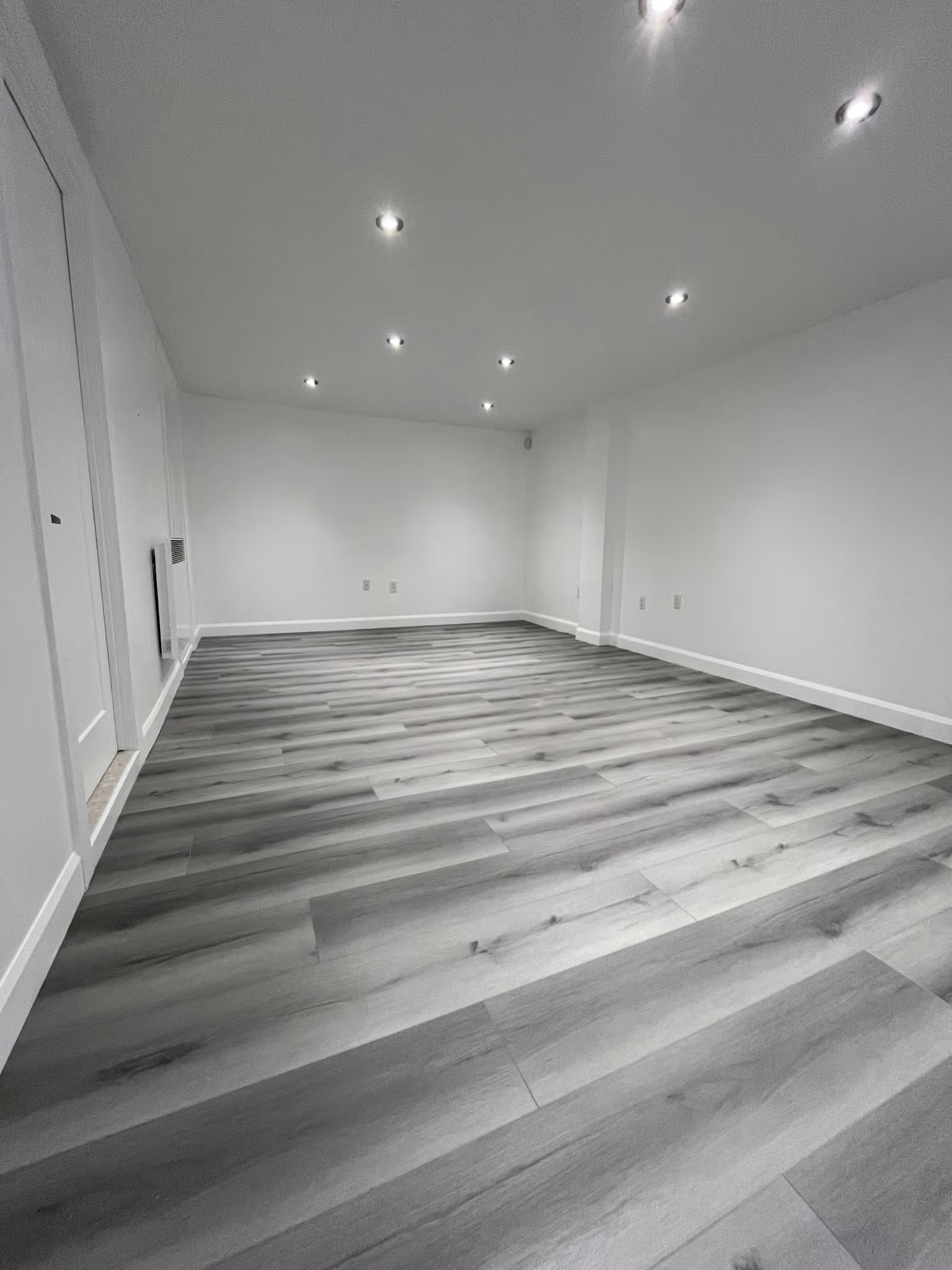 Sous-sol rénové avec plancher flottant gris moderne, murs blancs et éclairage encastré au plafond