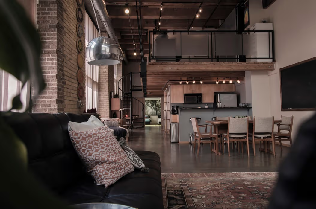 Loft industriel moderne avec mezzanine, mur de briques, escalier en colimaçon, cuisine ouverte, salle à manger et salon chaleureux.