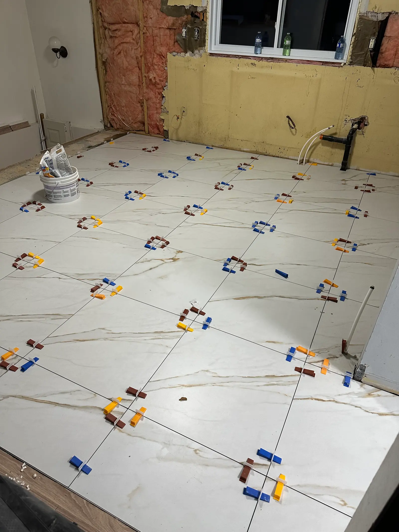 Marble-effect floor tile installation with leveling spacers in a room under renovation