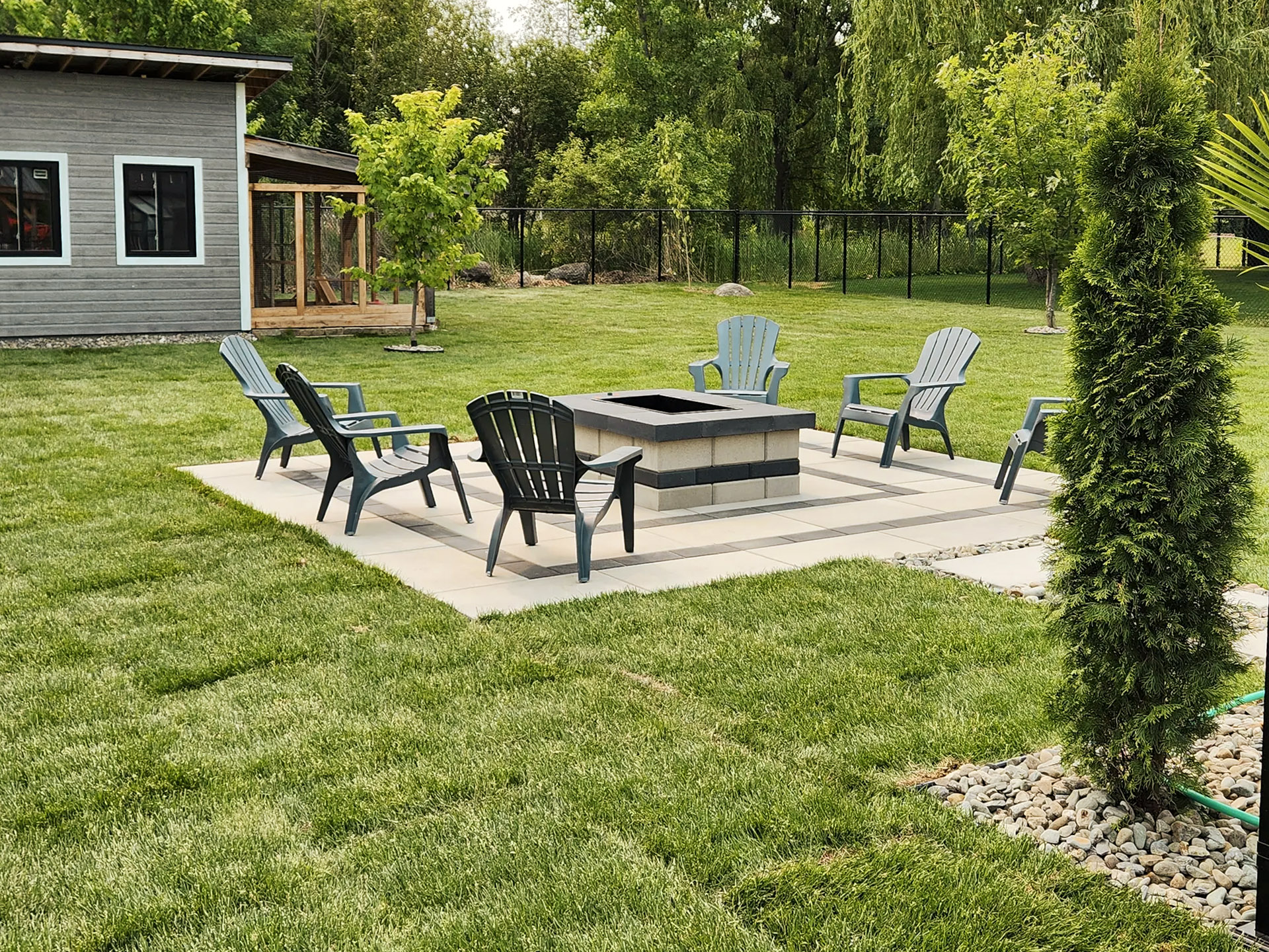 Outdoor living space with central fire pit, plastic chairs, and well-maintained lawn