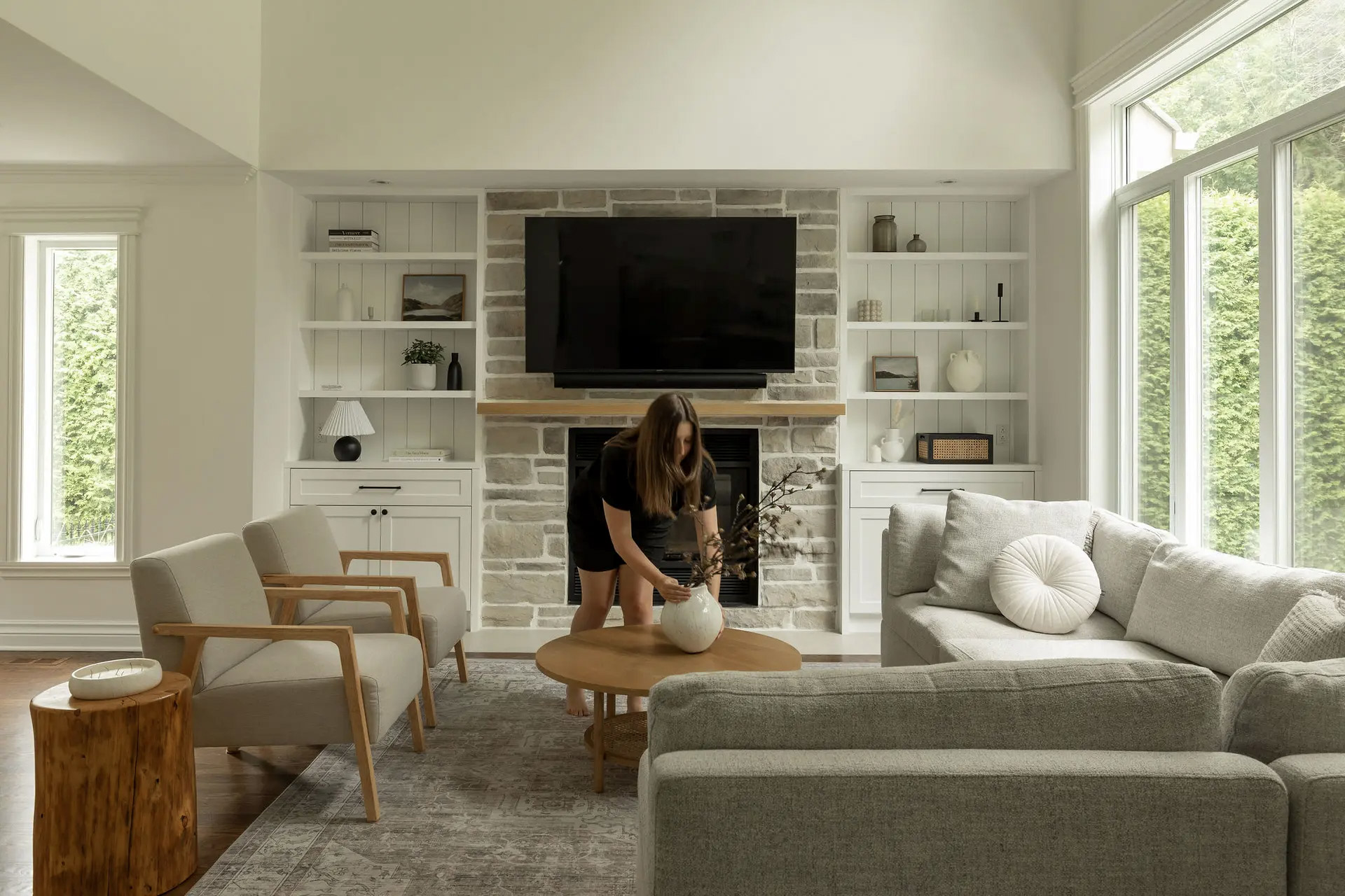 Salon lumineux avec foyer en pierres, mobilier scandinave, grande fenêtre et décoration minimaliste<br>