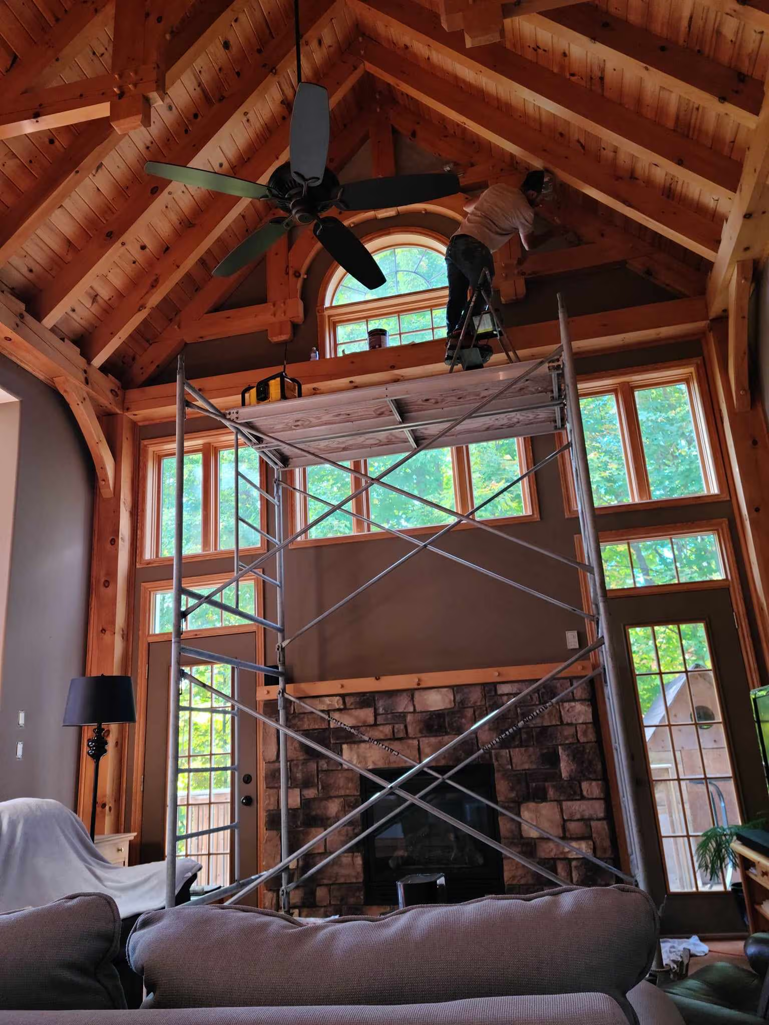 Travaux de rénovation dans un salon à plafond cathédrale avec charpente apparente en bois, échafaudage et ouvrier effectuant des réparations en hauteur