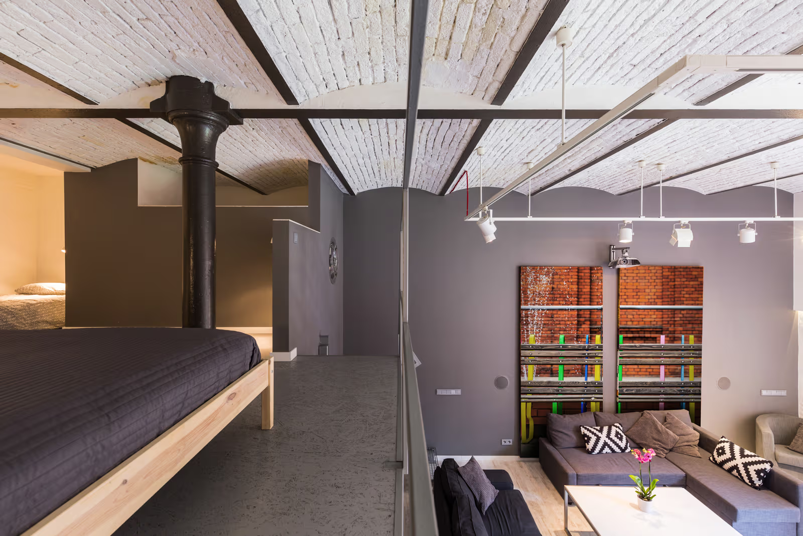 Mezzanine moderne avec chambre ouverte, plafond voûté en briques blanches, poutres métalliques noires et salon contemporain en contrebas.