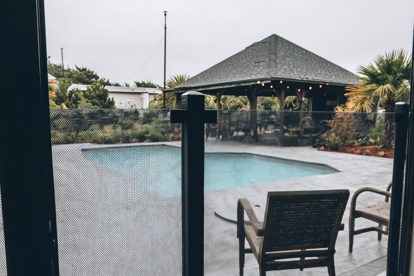 Inground pool with black mesh safety fence and concrete deck in a landscaped residential yard
