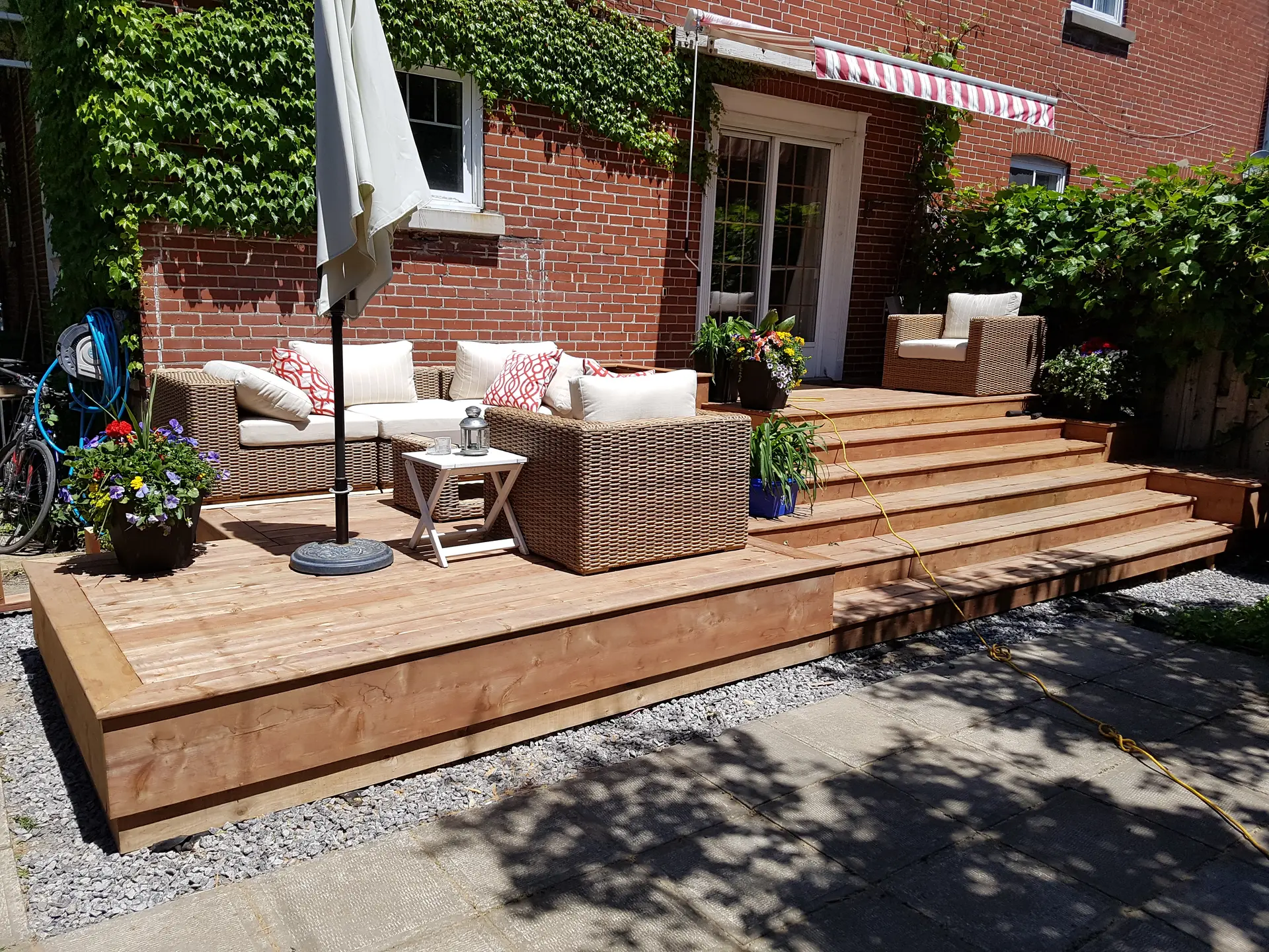 Wooden deck with wicker outdoor furniture and stairs in front of a red brick house