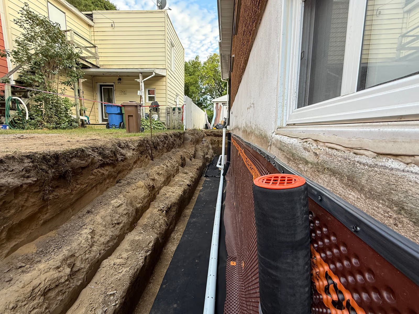 Residential foundation excavation with perforated French drain, waterproofing membrane, dimpled drainage board and trench along a house