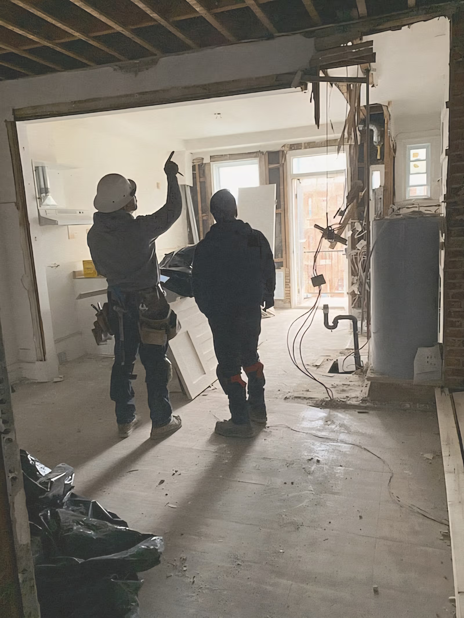 Workers on an interior renovation site with open walls, exposed electrical wires and visible structure