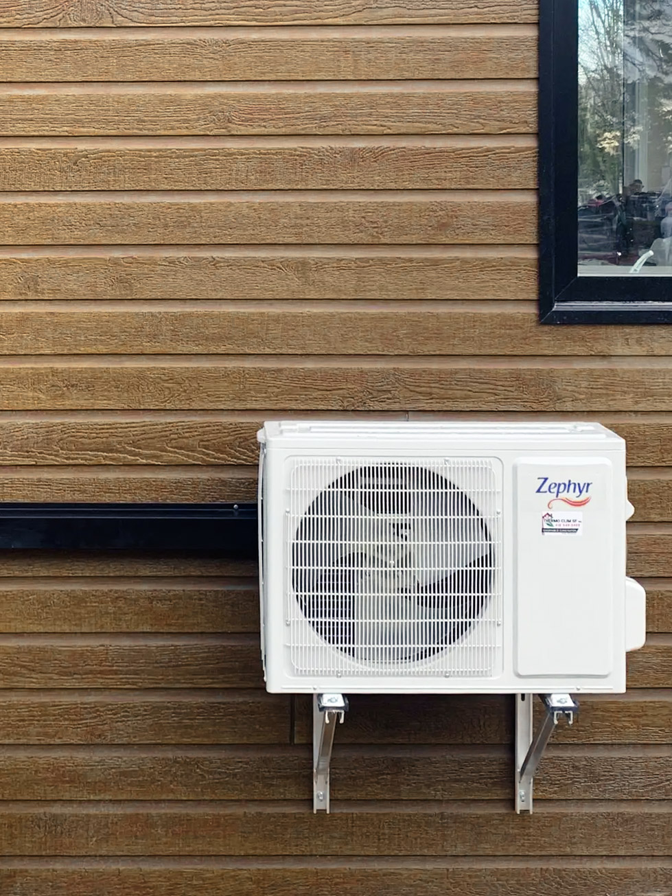 Zephyr outdoor air conditioning unit installed on a wood-clad wall.