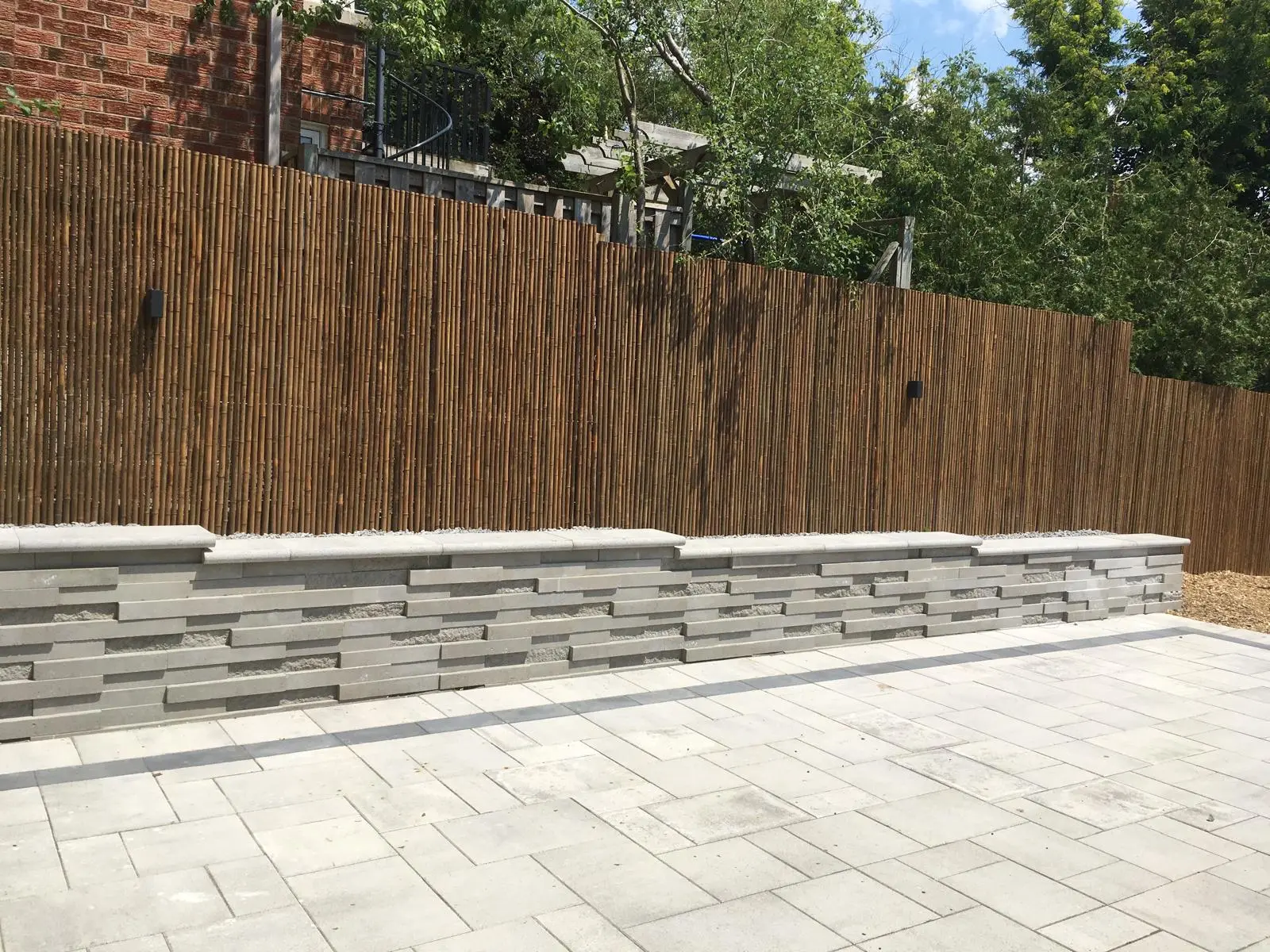 Muret moderne en blocs de béton gris avec patio en pavé uni et clôture en bois vertical&nbsp;