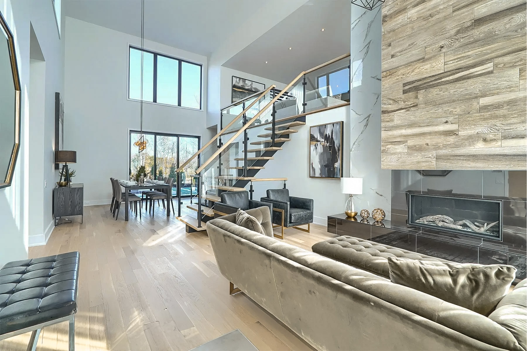 Salon moderne à aire ouverte avec escalier flottant, grandes fenêtres, foyer contemporain et plancher de bois clair