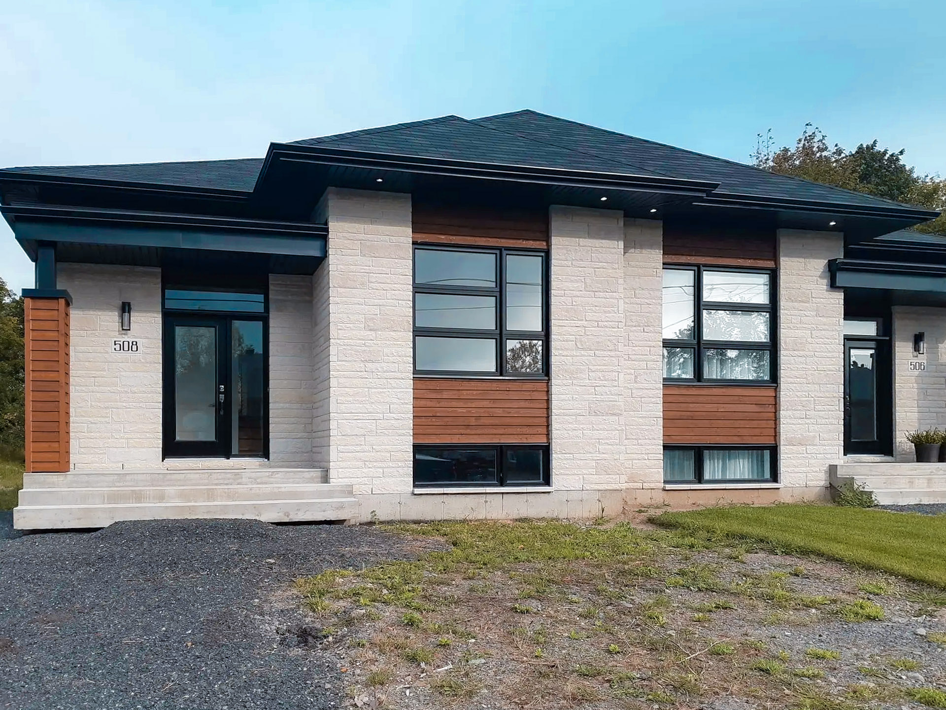 Facade of a modern duplex with light stone and wood cladding, black windows and a flat roof