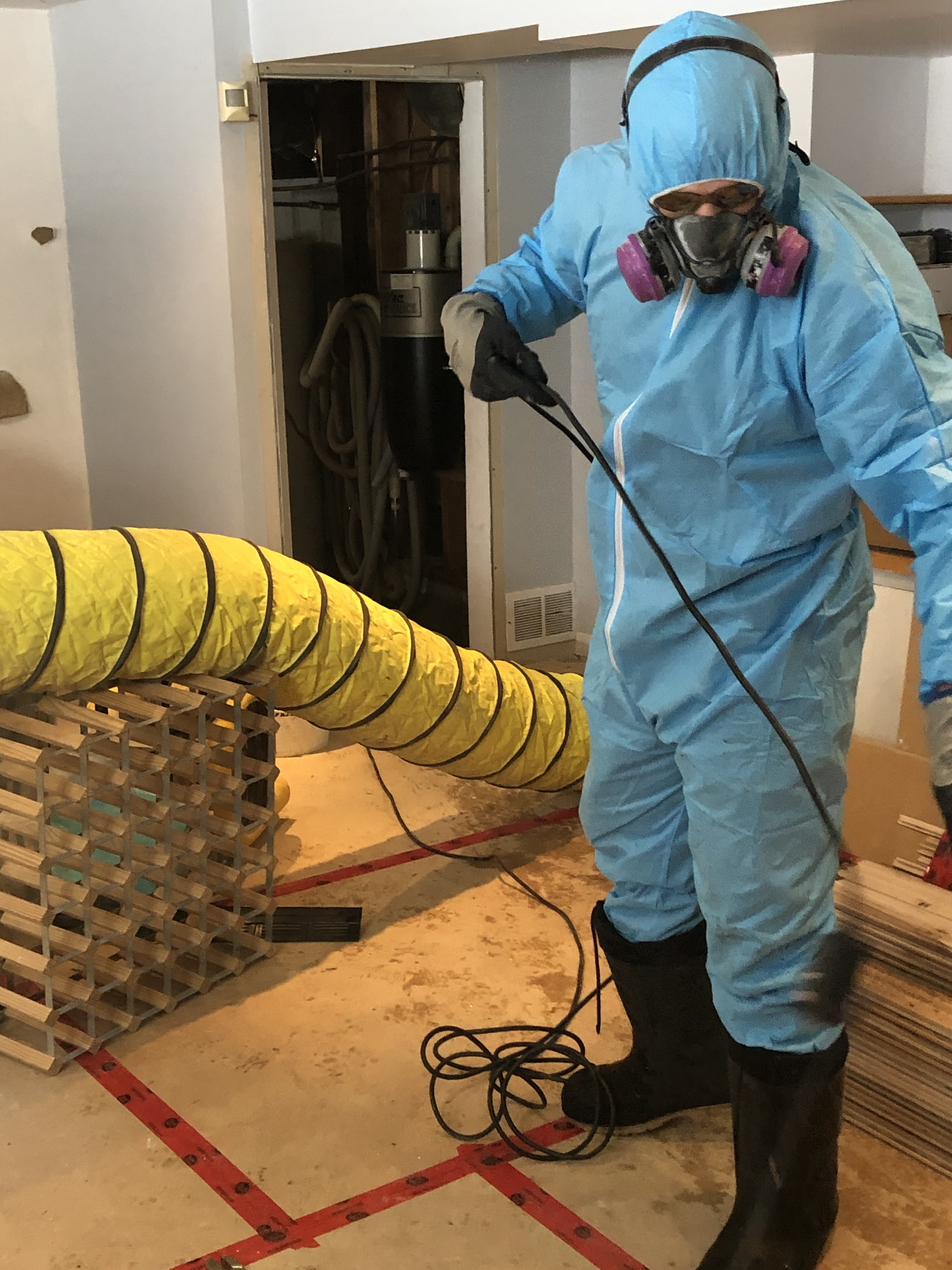 Technicien en combinaison de protection effectuant une décontamination intérieure avec équipement de ventilation et masque respiratoire