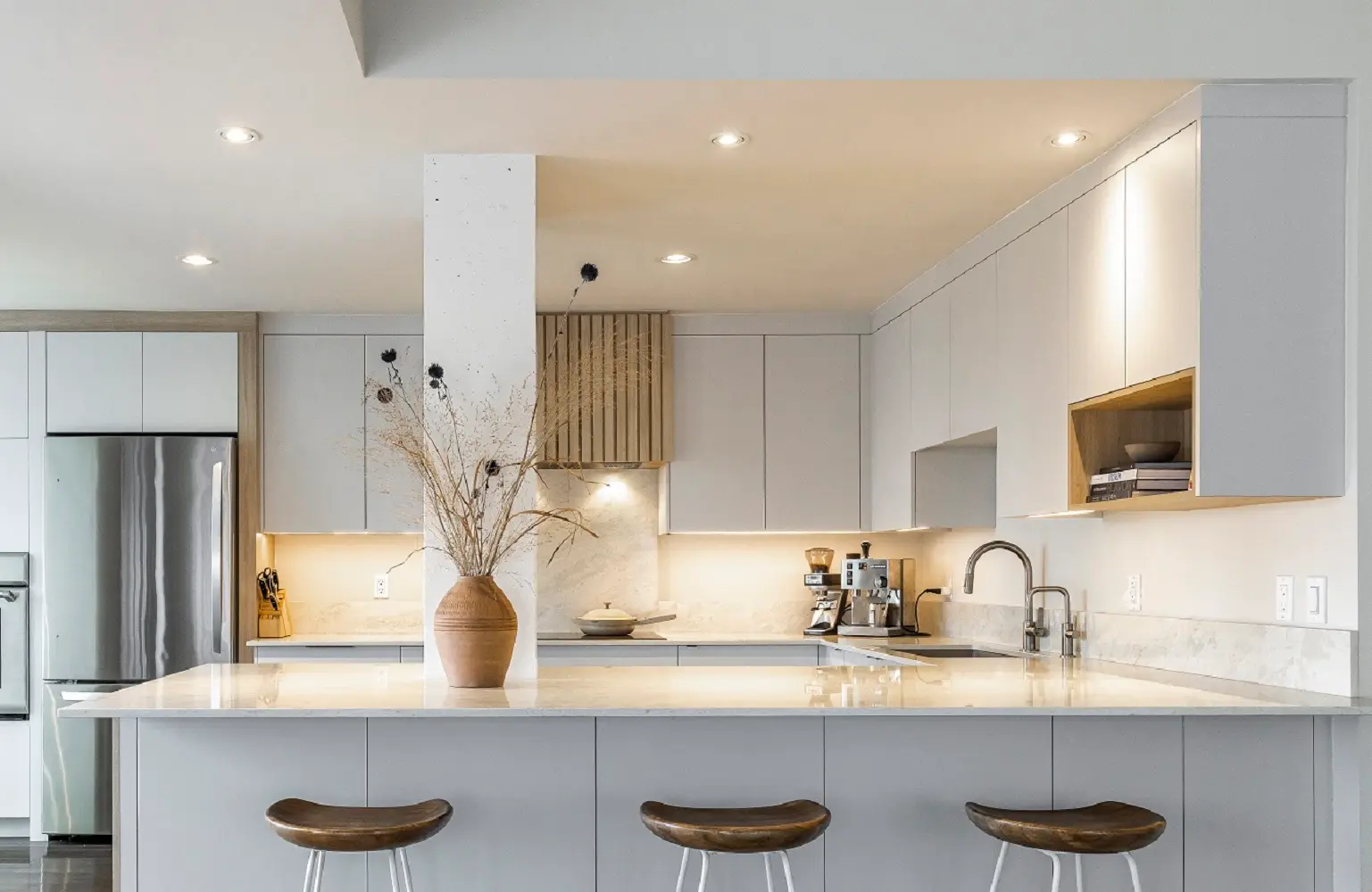 Cuisine moderne minimaliste avec îlot central blanc, armoires épurées, éclairage encastré et accents de bois naturel